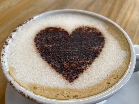 Schließen Sie Blick auf eine Kaffeetasse mit Schokoladenherz auf einen Cappuccino-Brennpunkt in der Mitte gestreut. Valentine.Love.Romance