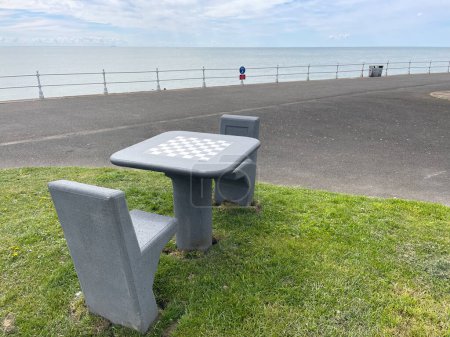 Zwei Sitze und ein Tisch mit einem Schachbrett, das an der Uferpromenade mit dem Meer im Hintergrund steht..