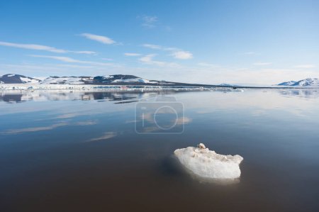 A wide low angle view of melting sea ice floes in still waters of Northern Arctic with mountains and tundra in background.Climate Crisis and Breakdown.Climate emergency