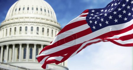 Téléchargez les photos : Le drapeau national des États-Unis agitant le vent avec le Capitole américain flou en arrière-plan. Illustration 3D rendu. Concentration sélective. Concept de démocratie et de patriotisme - en image libre de droit