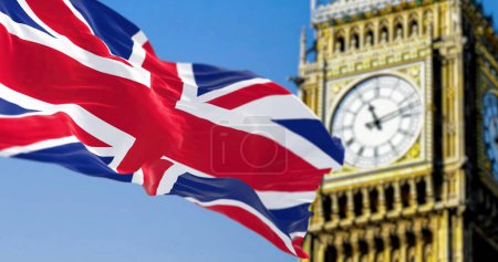 Téléchargez les photos : Drapeau national du Royaume-Uni agitant dans le vent avec Big Ben flou sur le fond. Illustration 3D rendu. Textile ondulé. Concentration sélective - en image libre de droit