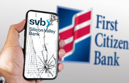 Photo for New York, US, March 2023: Hand holding a phone with Silicon Valley Bank logo on cracked screen. First Citizens Bank logo blurred on white background. Illustrative editorial - Royalty Free Image