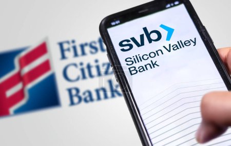 Photo for New York, US, March 2023: Hand holding a phone with Silicon Valley Bank logo on the screen with First Citizens Bank logo blurred on background. Illustrative editorial. Financial concept - Royalty Free Image
