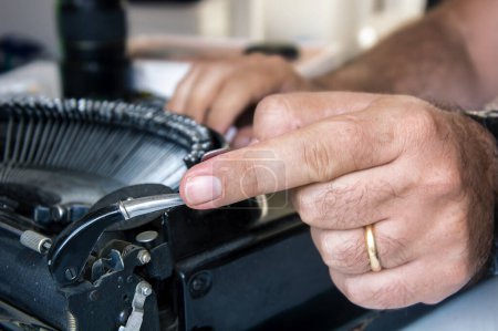 Téléchargez les photos : Gros plan de la main masculine actionnant le levier de retour du chariot sur une machine à écrire noire vintage. - en image libre de droit