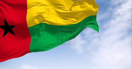 Foto de Bandera nacional de Guinea-Bissau ondeando en el viento en un día claro. Franja roja vertical, estrella negra izquierda, franjas horizontales amarillas y verdes derecha. 3d render ilustración. Tejido de aleteo - Imagen libre de derechos