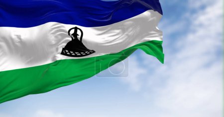 Foto de Bandera nacional de Lesotho ondeando en el viento en un día claro. Tres bandas horizontales de azul, blanco y verde con una gorra Basotho negra en el centro. 3d render ilustración. Tejido de aleteo - Imagen libre de derechos