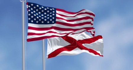 An einem sonnigen Tag wehen gemeinsam Flaggen der Vereinigten Staaten und Alabama. Die Flagge von Alabama zeigt ein rotes Kreuz auf einem weißen Feld. 3D Illustration Render, Flatternder Stoff. Selektiver Fokus