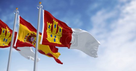 Flaggen von Kastilien-La Mancha und Spanien wehen an einem klaren Tag. Autonome Gemeinschaft von Spanien. 3D Illustration rendern. Selektiver Fokus. Wellenförmiges Gewebe