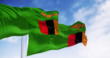 Drapeaux nationaux de Zambie agitant dans le vent par temps clair. Vert avec un aigle orange en vol sur un bloc de trois bandes verticales en rouge, noir et orange. Illustration 3D rendu
