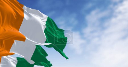 Drapeaux nationaux de Côte d'Ivoire agitant dans le vent par temps clair. Trois bandes verticales égales : orange, blanc et vert. Illustration 3D rendu. Tissu flottant