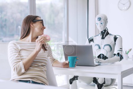 Téléchargez les photos : Travailleuse de bureau paresseuse mangeant des beignets et perdant du temps, elle regarde le robot IA efficace travailler avec un ordinateur portable - en image libre de droit