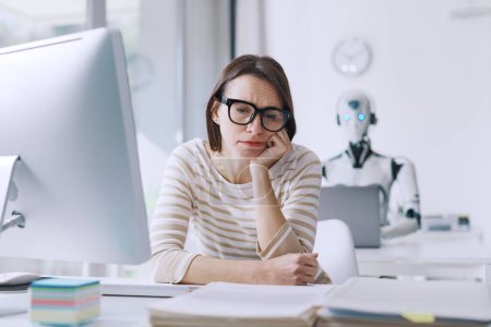 Foto de Decepcionada mujer de negocios estresada y robot AI sentado en su escritorio en la oficina, la mujer está preocupada y pensativa - Imagen libre de derechos