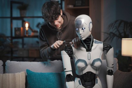 Téléchargez les photos : Adolescent intelligent réparant un robot IA dans le salon à la maison, concept de technologie et d'expertise - en image libre de droit