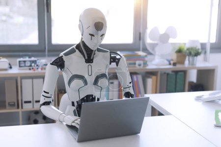 Téléchargez les photos : Un robot humanoïde travaille dans un bureau sur un ordinateur portable, montrant l'utilité de l'automatisation dans des tâches répétitives et fastidieuses. - en image libre de droit
