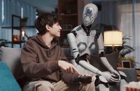 Téléchargez les photos : Adolescent heureux et robot AI assis sur le canapé à la maison, ils jouent à des jeux vidéo ensemble - en image libre de droit
