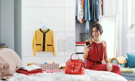 Téléchargez les photos : Femme à la mode débusquant sa garde-robe, elle prend des photos de son sac et le vend en ligne - en image libre de droit