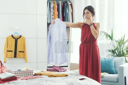 Photo for Elegant woman in her bedroom, she is decluttering her wardrobe and choosing clothes - Royalty Free Image