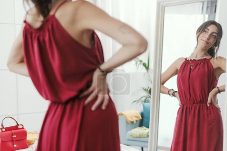 Téléchargez les photos : Femme confiante essayant une nouvelle tenue et se préparant à sortir, elle se regarde dans un miroir - en image libre de droit