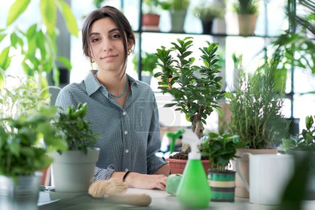 Téléchargez les photos : Jeune jardinier heureux posant à la maison et beaucoup de plantes luxuriantes - en image libre de droit