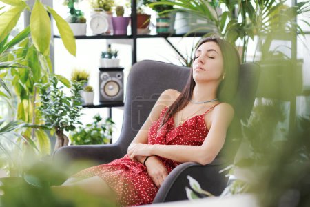 Téléchargez les photos : Jeune femme séduisante se relaxant à la maison entourée de belles plantes, elle dort sur un fauteuil - en image libre de droit
