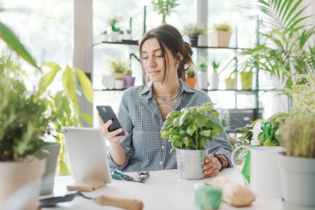 Foto de Mujer cuidando de sus hermosas plantas en casa, se está conectando en línea con su teléfono inteligente y la búsqueda de información - Imagen libre de derechos