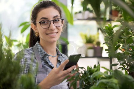 Foto de Floristería joven profesional que trabaja en su tienda, ella está tomando pedidos en línea en su teléfono inteligente - Imagen libre de derechos