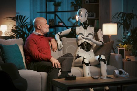 Senior-Mann und weiblicher KI-Roboter sitzen zu Hause auf der Couch und reden miteinander, Mensch-Roboter-Beziehungskonzept