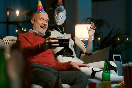 Foto de Solitario hombre mayor teniendo una fiesta en casa con su robot humanoide AI, se están tomando selfies con un teléfono inteligente - Imagen libre de derechos