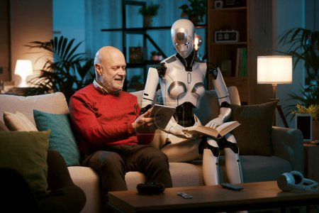 Foto de Feliz hombre mayor mostrando su tableta a un robot humanoide femenino, que están pasando tiempo juntos en casa - Imagen libre de derechos