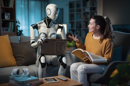 Foto de Una persona femenina disfrutando de su sala de estar inteligente, estudiando con un compañero de AI droid y portátil. - Imagen libre de derechos