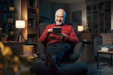 Photo for Happy senior man relaxing at home and connecting online with his digital tablet - Royalty Free Image