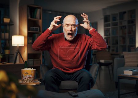 Photo for Senior man watching TV late at night, he is watching a scary horror movie - Royalty Free Image