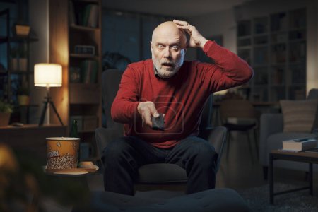 Téléchargez les photos : Homme âgé regardant la télévision tard dans la nuit, il regarde un film d'horreur effrayant - en image libre de droit