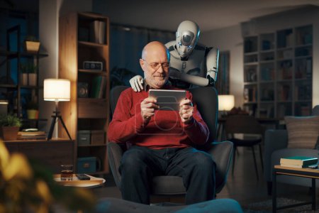 Téléchargez les photos : Heureux homme âgé regardant des vidéos sur sa tablette et robot IA humanoïde interactif debout à côté de lui - en image libre de droit