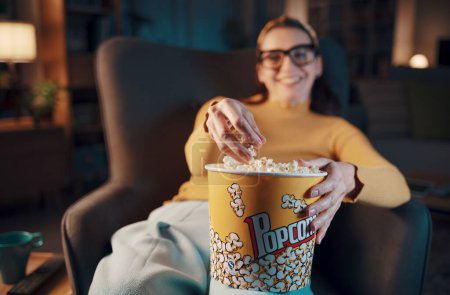 Foto de Mujer sonriente relajándose en casa, ella está viendo películas en la televisión y comiendo palomitas de maíz, mano de cerca - Imagen libre de derechos