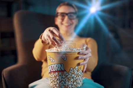 Photo for Smiling woman relaxing at home, she is watching movies on TV and eating popcorn, hand close up - Royalty Free Image