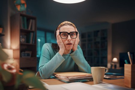 Foto de Mujer estresada en pánico sentada en su escritorio y revisando papeleo, facturas caras y facturas: finanzas caseras, concepto de deuda y presupuesto - Imagen libre de derechos
