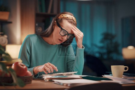 Foto de Mujer triste estresada comprobando facturas y facturas en casa, ella está calculando los costos con una calculadora - Imagen libre de derechos
