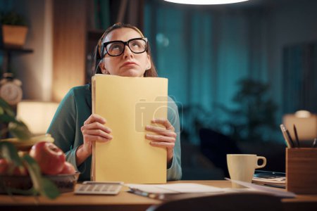 Téléchargez les photos : Femme frustrée assise à son bureau à la maison et vérifiant la paperasserie : finances à domicile, coûts et concept budgétaire - en image libre de droit