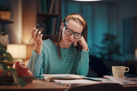 Photo for Bored woman checking bills and invoices at home, she is sitting at desk and reading paperwork - Royalty Free Image
