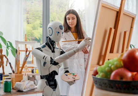 Foto de Artista mujer enseñando arte a un robot humanoide AI, ella está apuntando a lienzo y dando consejos - Imagen libre de derechos