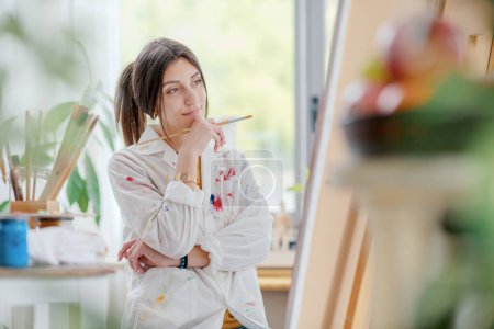 Foto de Joven artista femenina que trabaja en el estudio, está mirando su pintura y pensamiento, creatividad y concepto de arte - Imagen libre de derechos