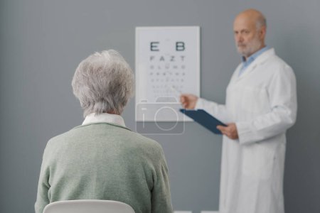 Foto de Mujer mayor que se somete a un examen ocular con un oculista profesional, ella está sentada y mirando la carta ocular - Imagen libre de derechos
