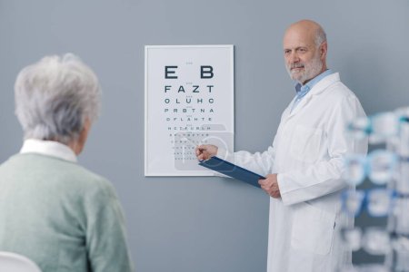Photo for Senior woman having an eye exam with a professional oculist, she is sitting and looking at the eye chart - Royalty Free Image