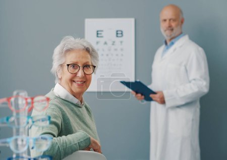 Photo for Senior woman having an eye exam with a doctor, they are smiling at camera - Royalty Free Image