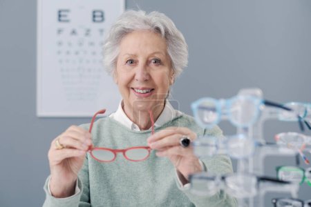 Seniorin wählt Brille im Brillengeschäft, sie hält Brille und lächelt