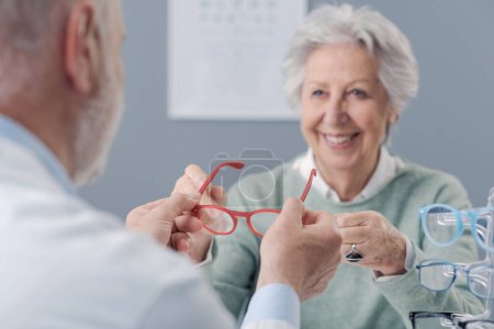 Photo for Smiling elderly woman trying new prescription glasses, the oculist is helping her - Royalty Free Image