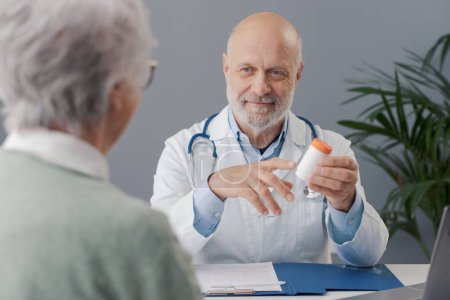 Téléchargez les photos : Docteur travaillant dans son bureau, il donne un médicament sur ordonnance à une femme âgée et souriant - en image libre de droit