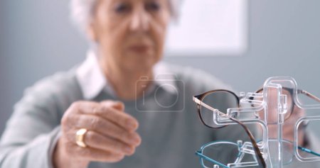 Téléchargez les photos : Femme âgée essayant de nouvelles lunettes chez l'opticien, concept de soins oculaires - en image libre de droit