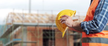 Photo for Building contractor holding a safety helmet and construction site in the background - Royalty Free Image